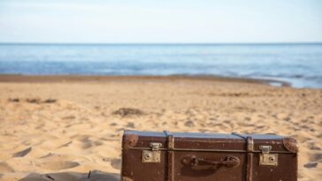 A vintage brown suitcase sits on a sandy beach, evoking travel and adventure.