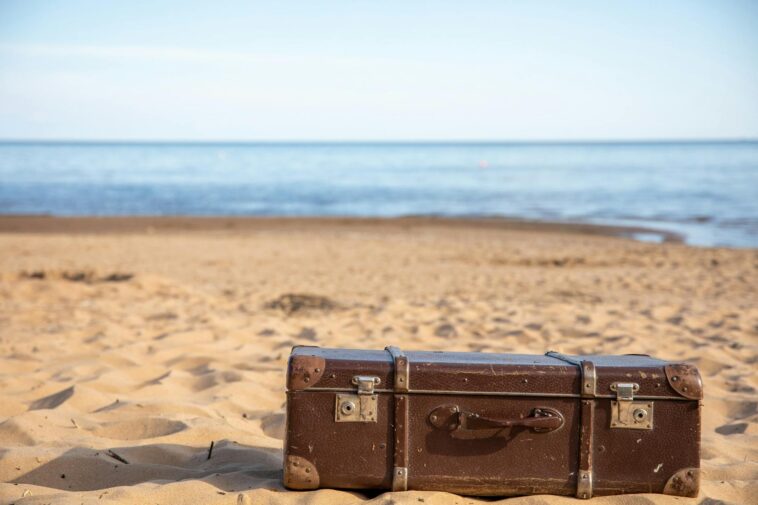 A vintage brown suitcase sits on a sandy beach, evoking travel and adventure.