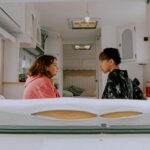 Two friends sit silently in a camper van, surrounded by a cozy interior.