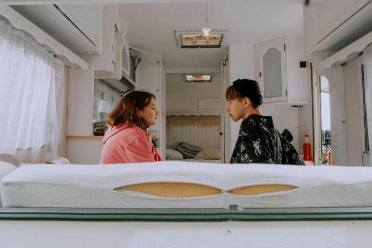 Two friends sit silently in a camper van, surrounded by a cozy interior.