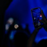 Fans recording a live concert with smartphones in a vibrant, colorful setting.