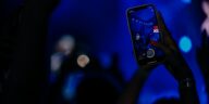 Fans recording a live concert with smartphones in a vibrant, colorful setting.