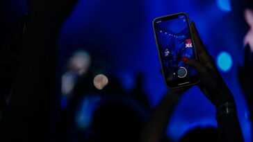 Fans recording a live concert with smartphones in a vibrant, colorful setting.
