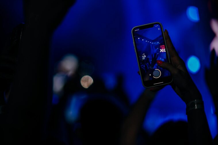 Fans recording a live concert with smartphones in a vibrant, colorful setting.