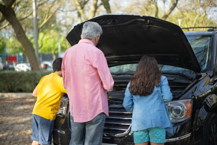Grandfather and grandchildren inspecting car engine on a sunny day in Portugal.