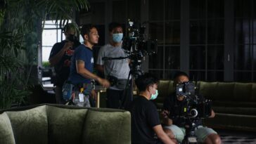 Film crew setting up camera equipment for indoor scene. Teamwork and filmmaking in action.