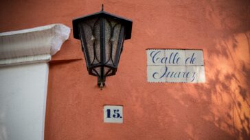 A street light casting shadows over a 'Calle de Juarez' sign and address number in Mexico City.