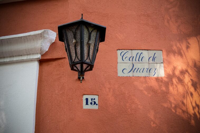 A street light casting shadows over a 'Calle de Juarez' sign and address number in Mexico City.