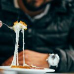 Close-up of a man enjoying a cheesy meal in a cozy restaurant setting.