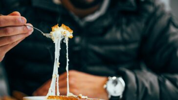 Close-up of a man enjoying a cheesy meal in a cozy restaurant setting.