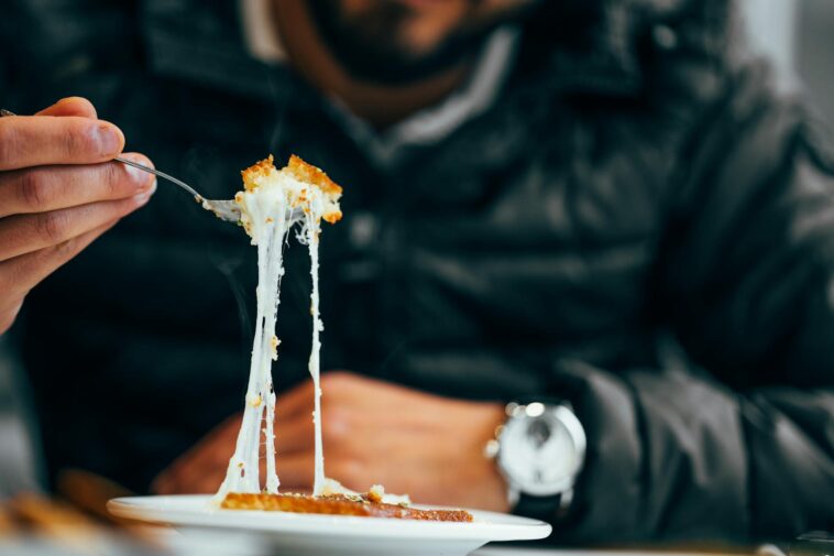 Close-up of a man enjoying a cheesy meal in a cozy restaurant setting.