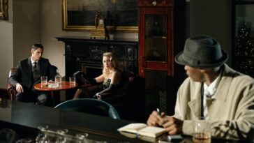 A detective watches a conversation unfold in a vintage lounge, capturing the essence of noir fiction.