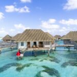 Overwater villa with couple in red dress in a tropical paradise setting.