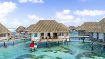 Overwater villa with couple in red dress in a tropical paradise setting.