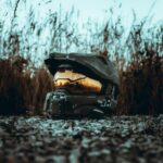 A futuristic helmet with a reflective visor placed outdoors on rocky ground, bathed in sunset light.