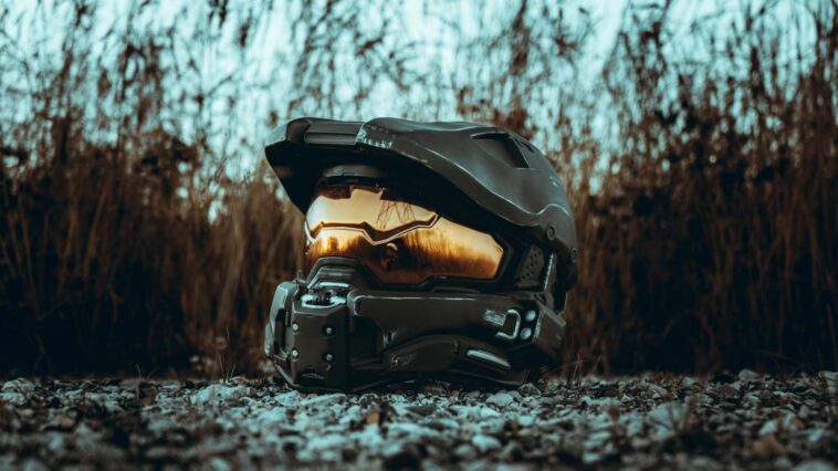 A futuristic helmet with a reflective visor placed outdoors on rocky ground, bathed in sunset light.