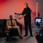 Professional film set with actor in suit, director using clapperboard.