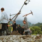 Film crew setting up a historical scene with actors outdoors in nature.