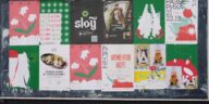 Colorful urban bulletin board with various artistic posters in multiple languages.
