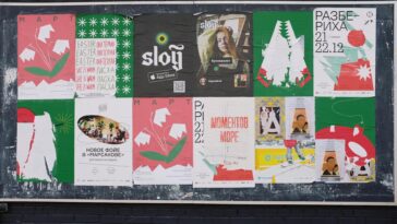 Colorful urban bulletin board with various artistic posters in multiple languages.