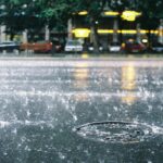 Vibrant rain scene on a Bucharest city street, showcasing splashing water and a lively urban atmosphere.