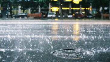 Vibrant rain scene on a Bucharest city street, showcasing splashing water and a lively urban atmosphere.