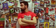 Portrait of a bearded man in a red t-shirt surrounded by vintage movie DVDs, showcasing a love for cinema.