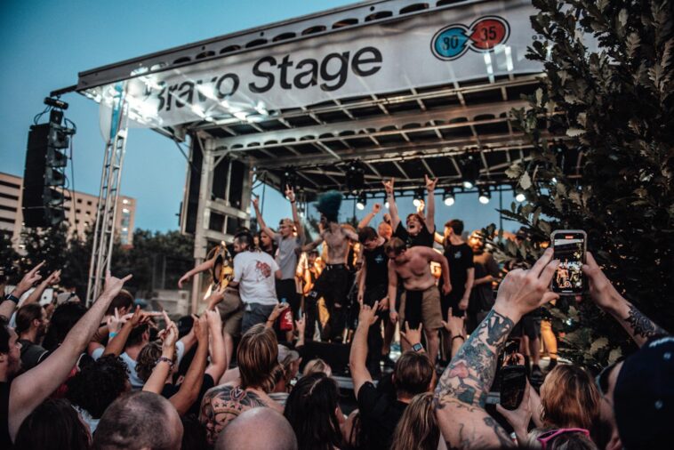 A lively outdoor concert scene with a diverse crowd enjoying the music under bright stage lights.