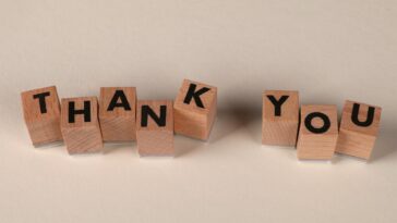 Wooden blocks spell 'THANK YOU' on a soft beige background, expressing gratitude.
