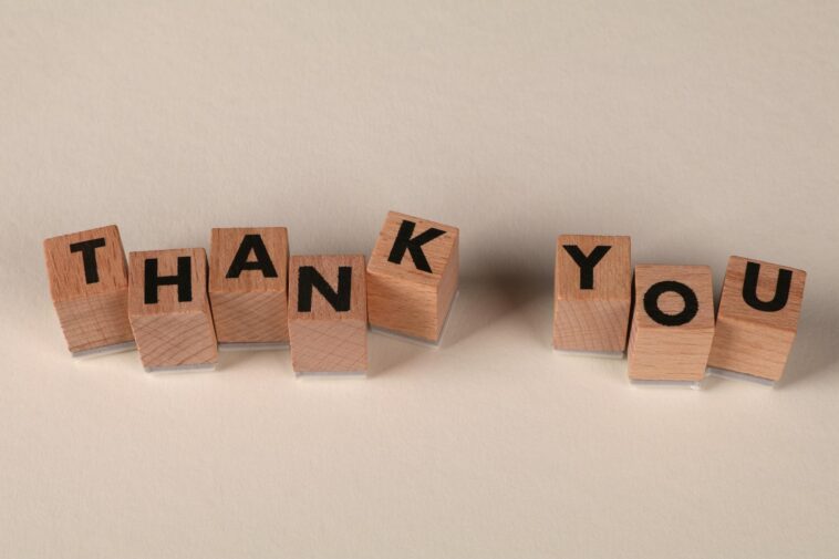 Wooden blocks spell 'THANK YOU' on a soft beige background, expressing gratitude.