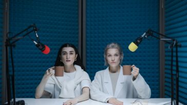 Two women in a soundproof podcast studio holding mugs next to microphones