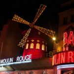 Brightly illuminated Moulin Rouge windmill in Paris at night.