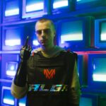 Man with prosthetic arm stands confidently in front of retro televisions, showcasing modern technology.