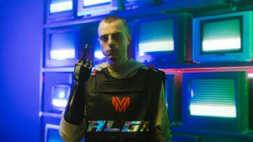 Man with prosthetic arm stands confidently in front of retro televisions, showcasing modern technology.