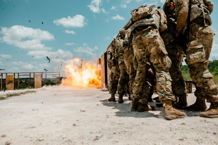 Soldiers in camouflage uniforms near a controlled explosion during training.
