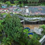 Aerial shot of a unique abandoned building with a rooftop garden surrounded by lush trees.