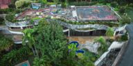 Aerial shot of a unique abandoned building with a rooftop garden surrounded by lush trees.