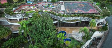 Aerial shot of a unique abandoned building with a rooftop garden surrounded by lush trees.