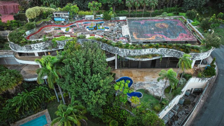 Aerial shot of a unique abandoned building with a rooftop garden surrounded by lush trees.