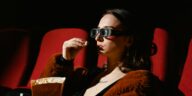 A woman enjoying a cinema experience wearing 3D glasses, holding popcorn.