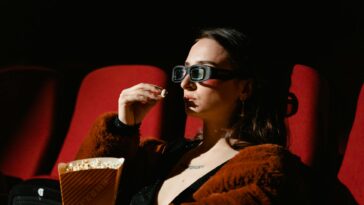 A woman enjoying a cinema experience wearing 3D glasses, holding popcorn.