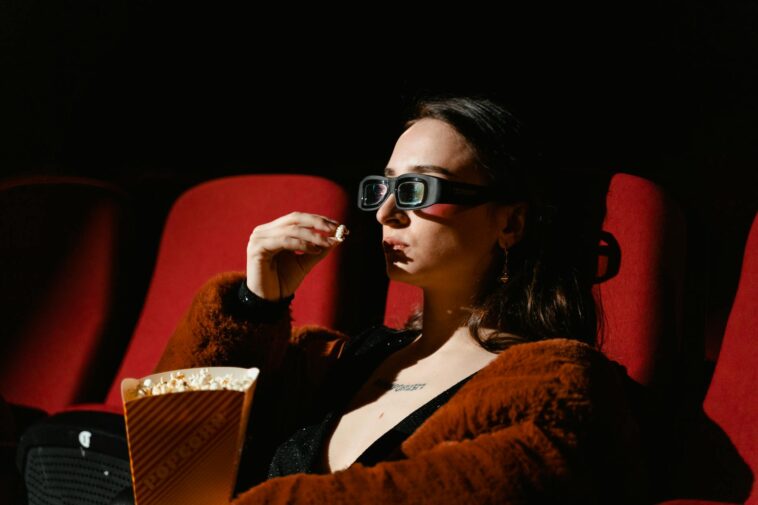 A woman enjoying a cinema experience wearing 3D glasses, holding popcorn.