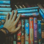 A hand reaching for a classic VHS tape from a colorful vintage collection indoors.
