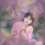 Young woman in a pink dress surrounded by beautiful pink flowers, creating a serene and dreamy atmosphere.