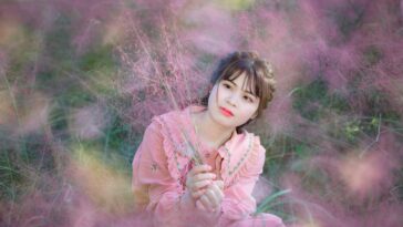 Young woman in a pink dress surrounded by beautiful pink flowers, creating a serene and dreamy atmosphere.