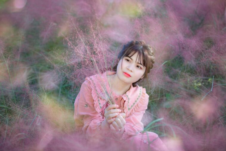Young woman in a pink dress surrounded by beautiful pink flowers, creating a serene and dreamy atmosphere.