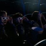 Group of teenagers wearing 3D glasses in a cinema with popcorn during a movie.