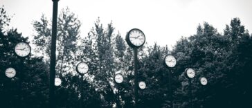 A collection of clocks set against a backdrop of trees in a park, creating a surreal scene.