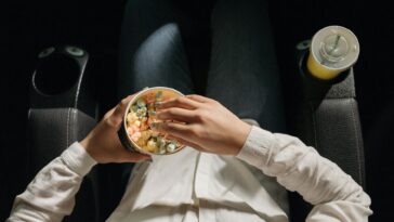 Close-up of a person holding colorful popcorn in a cinema seat.