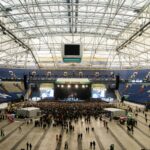 Wide shot of a crowded concert in a large indoor arena with a prominent stage.